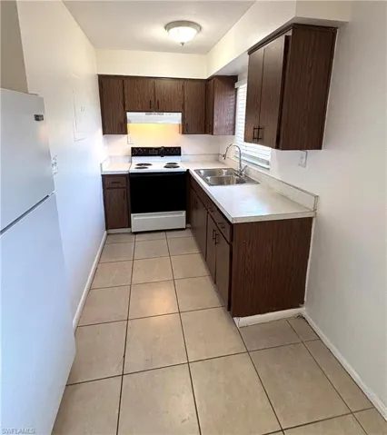 Kitchen featuring white appliances, light countertops, dark wood finish cabinets, and light tile patterned flooring