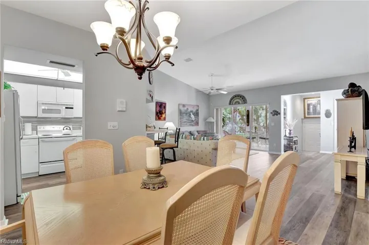 Dining space with light wood-style floors, ceiling fan, vaulted ceiling, and a chandelier