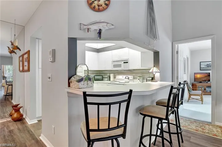 Kitchen featuring wood finished floors, a breakfast bar, backsplash, light countertops, and white cabinets