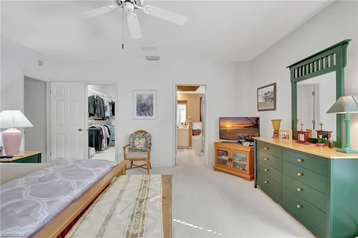Bedroom featuring light colored carpet, a walk in closet, ceiling fan, and connected bathroom