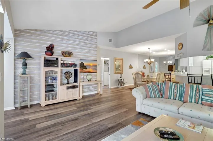 Living room featuring vaulted ceiling, wood finished floors, a chandelier, and a ceiling fan