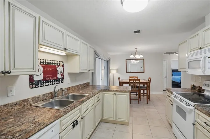 Kitchen with white appliances, a chandelier, a peninsula, dark countertops, and light tile patterned floors