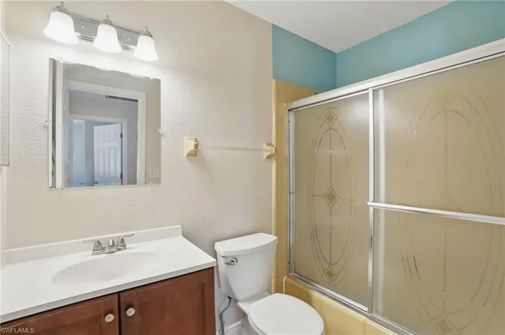 Full bathroom featuring a textured wall, shower / bath combination with glass door, and vanity