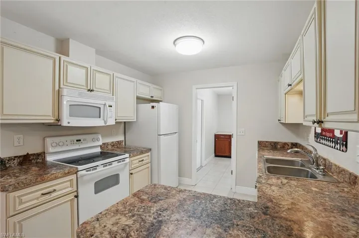 Kitchen with white appliances, cream cabinetry, and light tile patterned floors