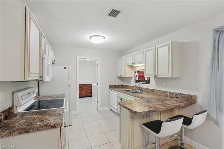 Kitchen featuring dark countertops, white appliances, a peninsula, and a kitchen bar