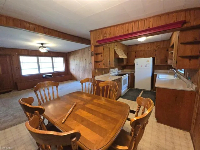 Dining room featuring sink, wood walls, light carpet, and ceiling fan