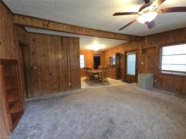 Unfurnished living room with ceiling fan, light carpet, and wooden walls