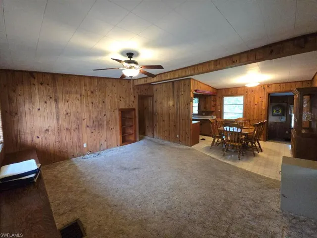 Unfurnished living room featuring ceiling fan, wooden walls, and carpet flooring