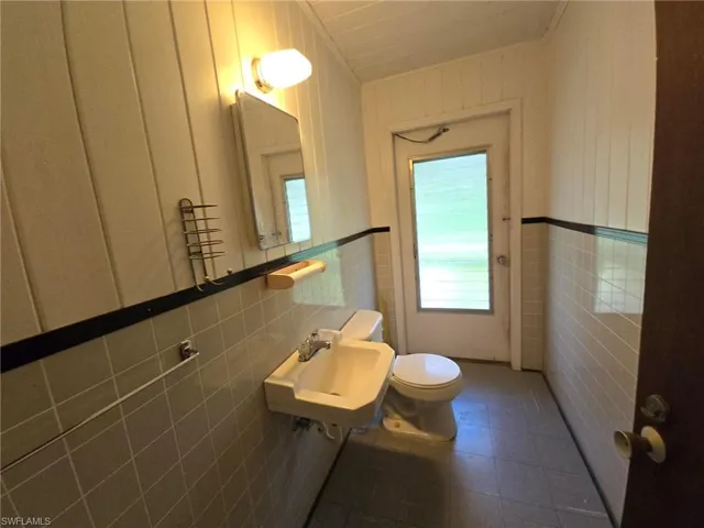 Bathroom featuring tile walls, tile patterned floors, toilet, and sink
