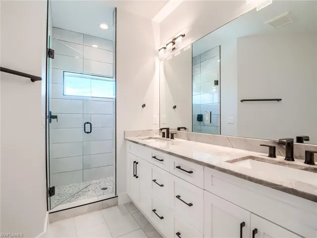 Bathroom with dual sinks, tile flooring, vanity with extensive cabinet space, and a shower with shower door