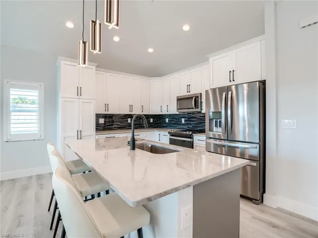 Kitchen with appliances with stainless steel finishes, hanging light fixtures, tasteful backsplash, and light wood-type flooring
