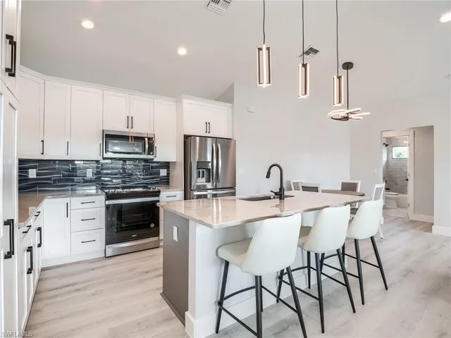 Kitchen featuring decorative light fixtures, stainless steel appliances, a center island with sink, light wood-type flooring, and sink