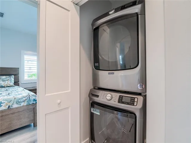 Laundry room with stacked washer and clothes dryer and light wood-type flooring