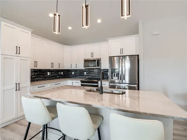 Kitchen with a center island with sink, light wood-type flooring, decorative light fixtures, and appliances with stainless steel finishes