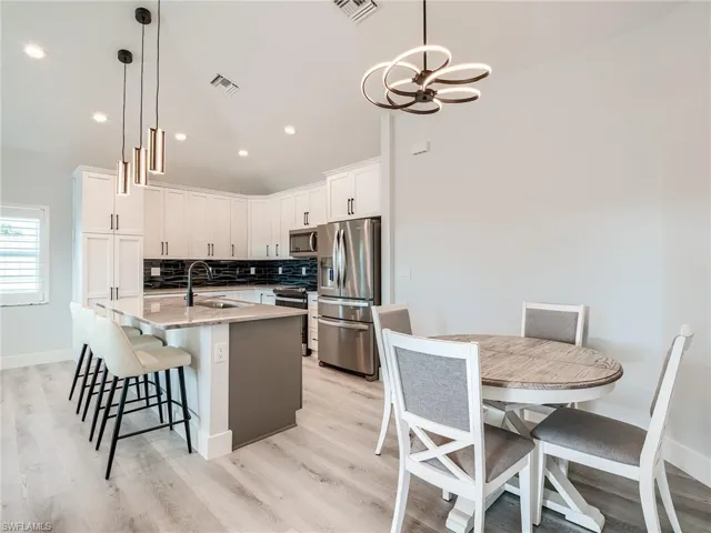 Kitchen featuring decorative light fixtures, light hardwood / wood-style floors, tasteful backsplash, appliances with stainless steel finishes, and sink