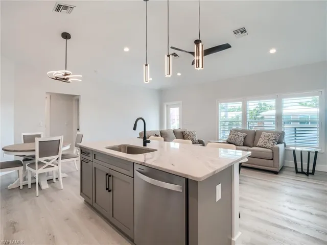 Kitchen featuring light stone countertops, light hardwood / wood-style floors, stainless steel dishwasher, an island with sink, and sink