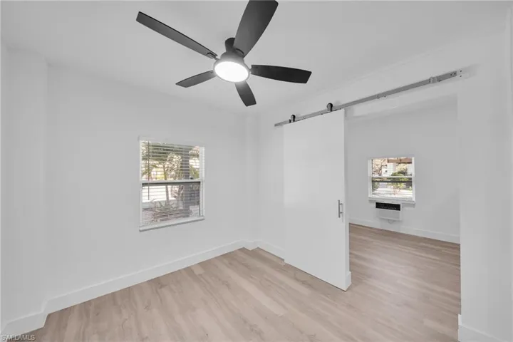Empty room with a barn door, light wood finished floors, and a ceiling fan