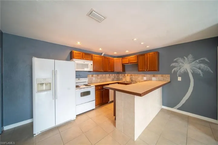 Kitchen featuring white appliances, a peninsula, tasteful backsplash, wood finish cabinetry, and light tile patterned floors