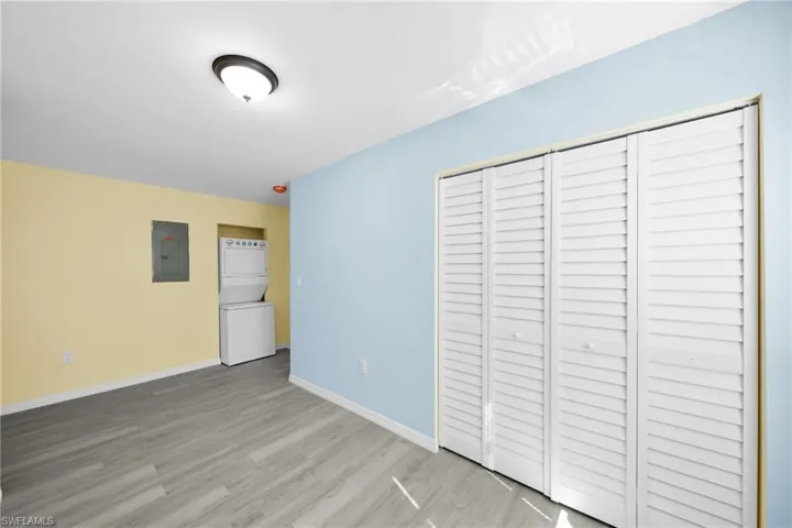 Unfurnished bedroom with a closet, stacked washer and clothes dryer, electric panel, and light wood-style flooring