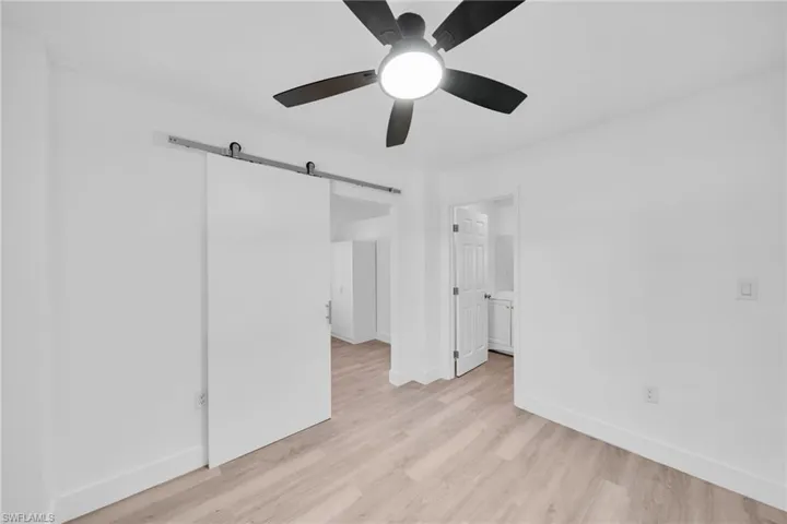 Unfurnished bedroom featuring a barn door, light wood-type flooring, and ceiling fan