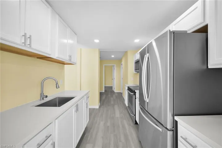 Kitchen with white cabinetry, recessed lighting, stainless steel appliances, light wood finished floors, and light stone countertops