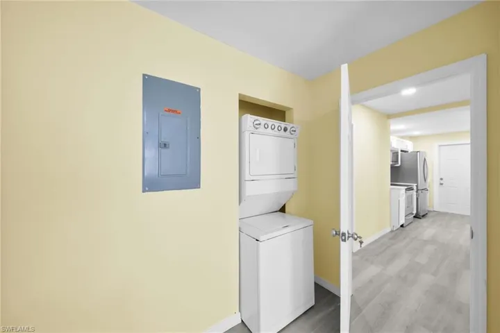 Laundry area featuring electric panel, stacked washer / dryer, and light wood-type flooring