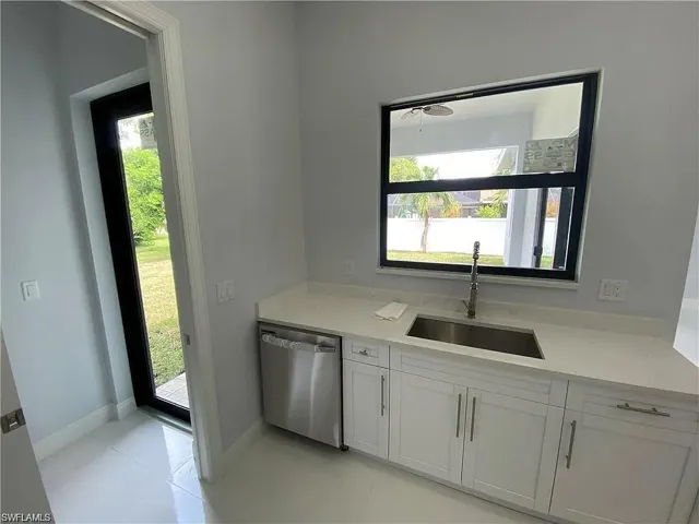 Kitchen featuring stainless steel dishwasher, white cabinets, light stone countertops, and light tile patterned floors