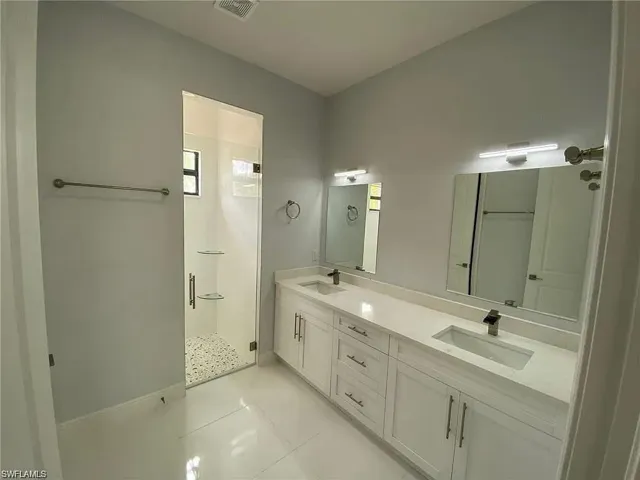 Bathroom featuring double vanity, a shower stall, and light tile patterned flooring