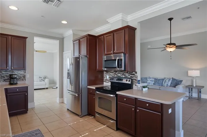 Kitchen with stainless steel appliances, tasteful backsplash, light countertops, ornamental molding, and light tile patterned floors