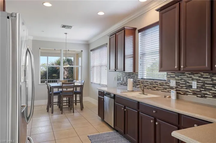 Kitchen with appliances with stainless steel finishes, crown molding, light tile patterned flooring, dark brown cabinetry, and plenty of natural light