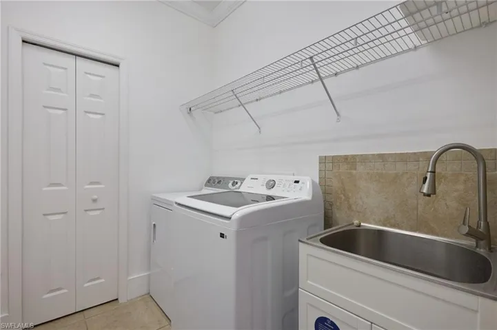 Washroom featuring light tile patterned floors, ornamental molding, and washing machine and dryer