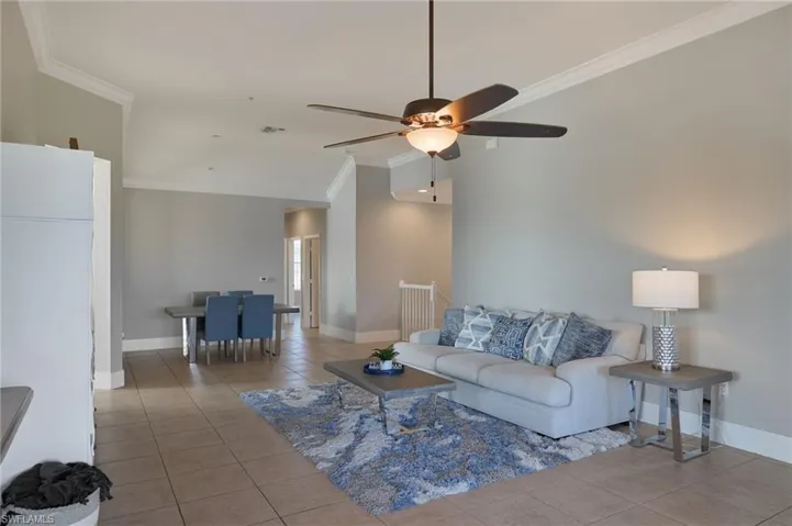 Living area with light tile patterned floors, crown molding, ceiling fan, and lofted ceiling