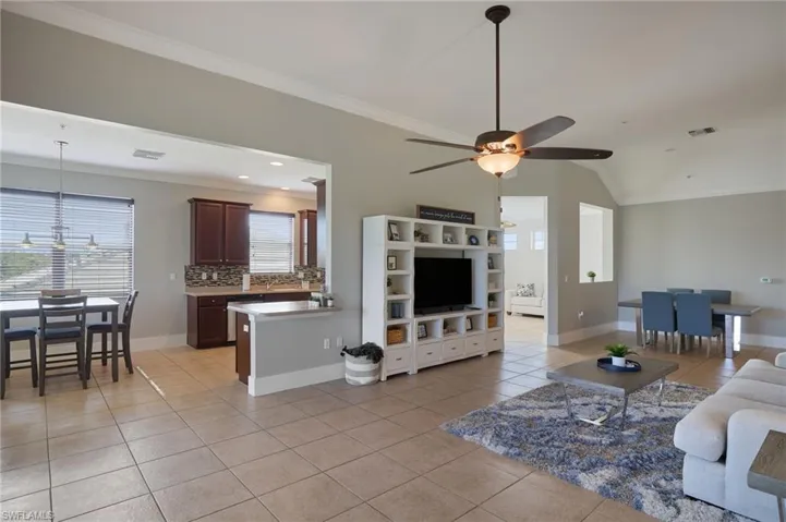 Living room featuring ornamental molding, light tile patterned flooring, lofted ceiling, ceiling fan, and recessed lighting