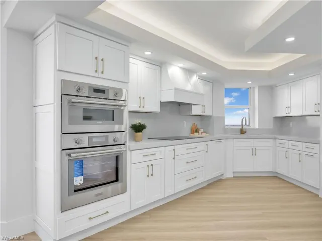Kitchen featuring double oven, custom exhaust hood, black electric cooktop, light countertops, and white cabinets