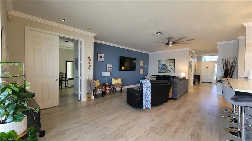 Living room with wood-type flooring, ornamental molding, ceiling fan, and a textured ceiling