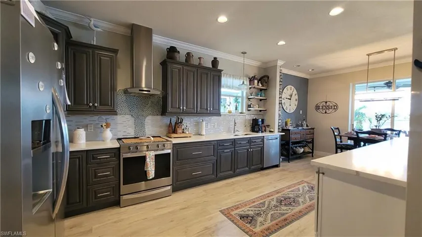 Kitchen with wall chimney range hood, stainless steel appliances, a wealth of natural light, and light wood-type flooring