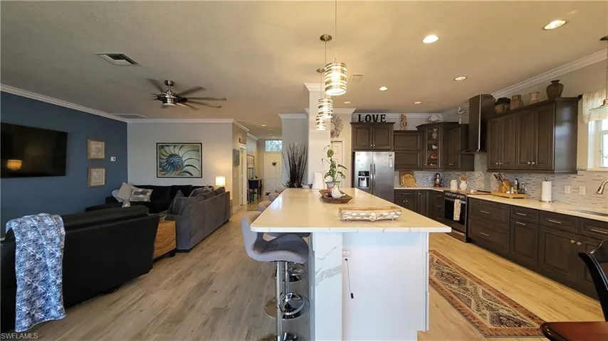 Kitchen featuring a center island, wall chimney range hood, light wood-type flooring, appliances with stainless steel finishes, and dark brown cabinets