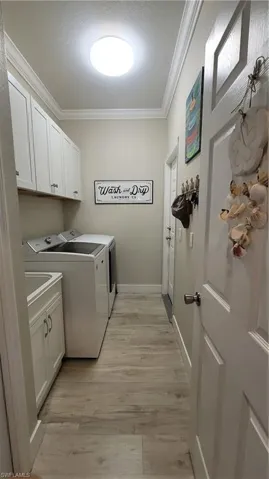 Laundry area featuring washer and dryer, cabinets, a textured ceiling, ornamental molding, and light hardwood / wood-style flooring