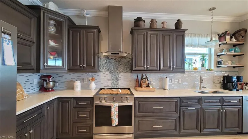 Kitchen featuring wall chimney range hood, stainless steel appliances, tasteful backsplash, and sink
