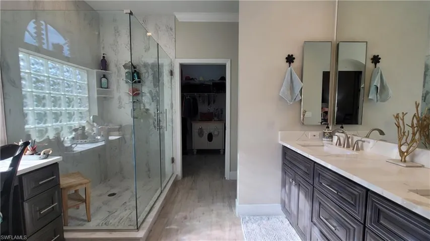 Bathroom featuring an enclosed shower, ornamental molding, wood-type flooring, and vanity with extensive cabinet space