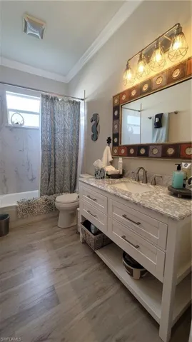 Full bathroom with hardwood / wood-style flooring, toilet, ornamental molding, vanity, and shower / bath combo