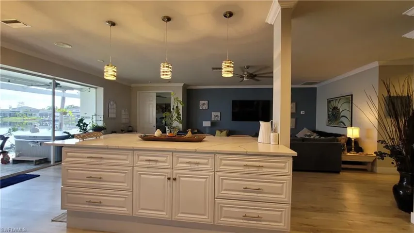 Kitchen with light hardwood / wood-style floors, light stone countertops, crown molding, hanging light fixtures, and ceiling fan