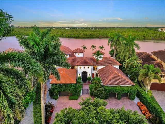 Mediterranean-style residence featuring a terracotta tile roof, white stucco exterior, and lush tropical landscaping