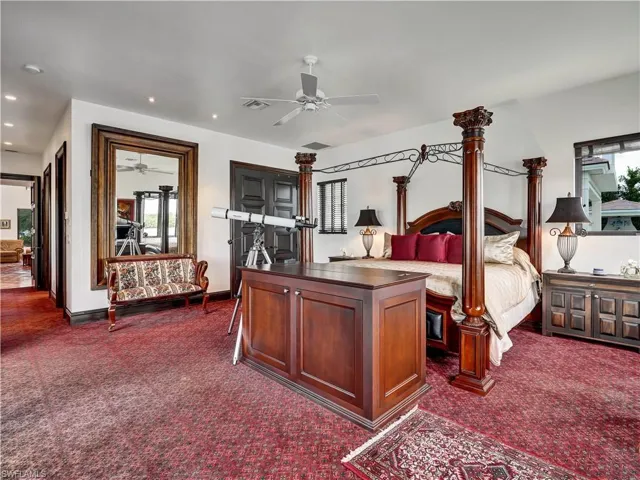 Spacious room featuring red patterned carpeting, a ceiling fan, recessed lighting, a large wall mirror with a carved wood frame, and a dark wood four-poster bed