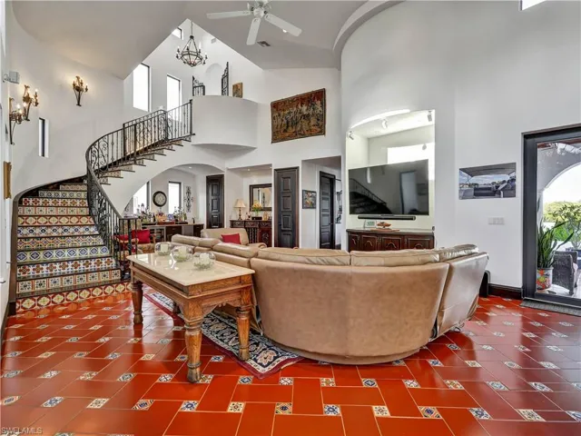 Grand entry featuring a custom wrought iron spiral staircase with patterned tile risers, terracotta tile flooring with accent tiles, and a double-height ceiling