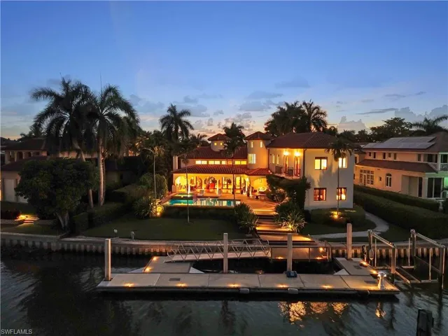 Mediterranean-style residence featuring a terracotta tile roof, private swimming pool, waterfront access with a substantial dock, integrated boat lifts, and mature palm landscaping