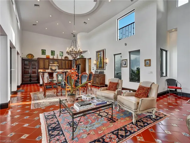 Spacious living area featuring terra cotta tile flooring with decorative inserts, a grand chandelier, and a recessed ceiling dome