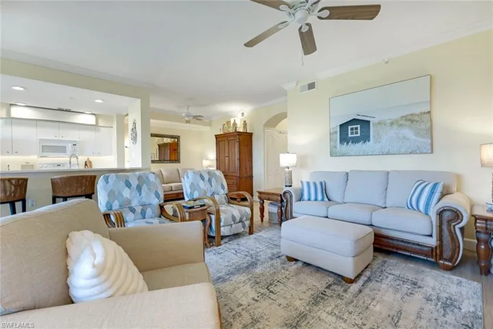 Living room with arched walkways, crown molding, and a ceiling fan