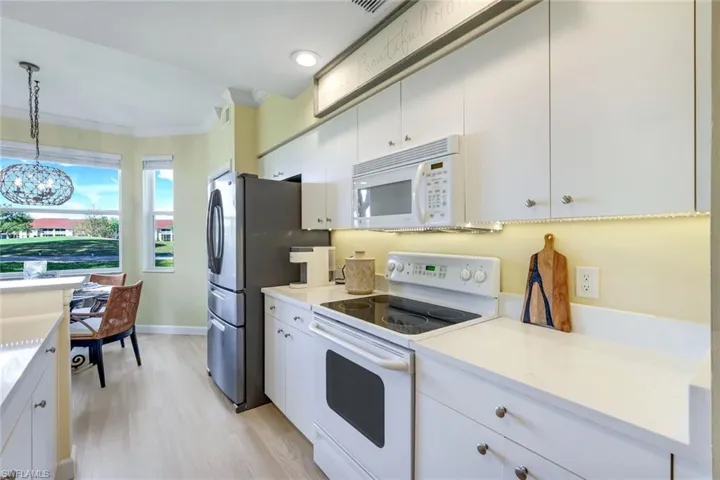 Kitchen with light countertops, crown molding, white appliances, white cabinetry, and decorative light fixtures