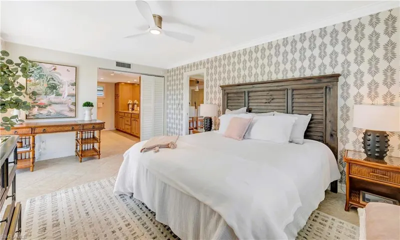 Primary bedroom featuring king-size bed, light tile floors, ornamental molding, ceiling fan, and ensuite bathroom